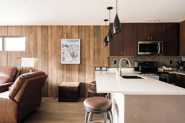 Una cocina moderna con paneles de madera, una isla grande, electrodomésticos de acero inoxidable y un salpicadero de piedra.
