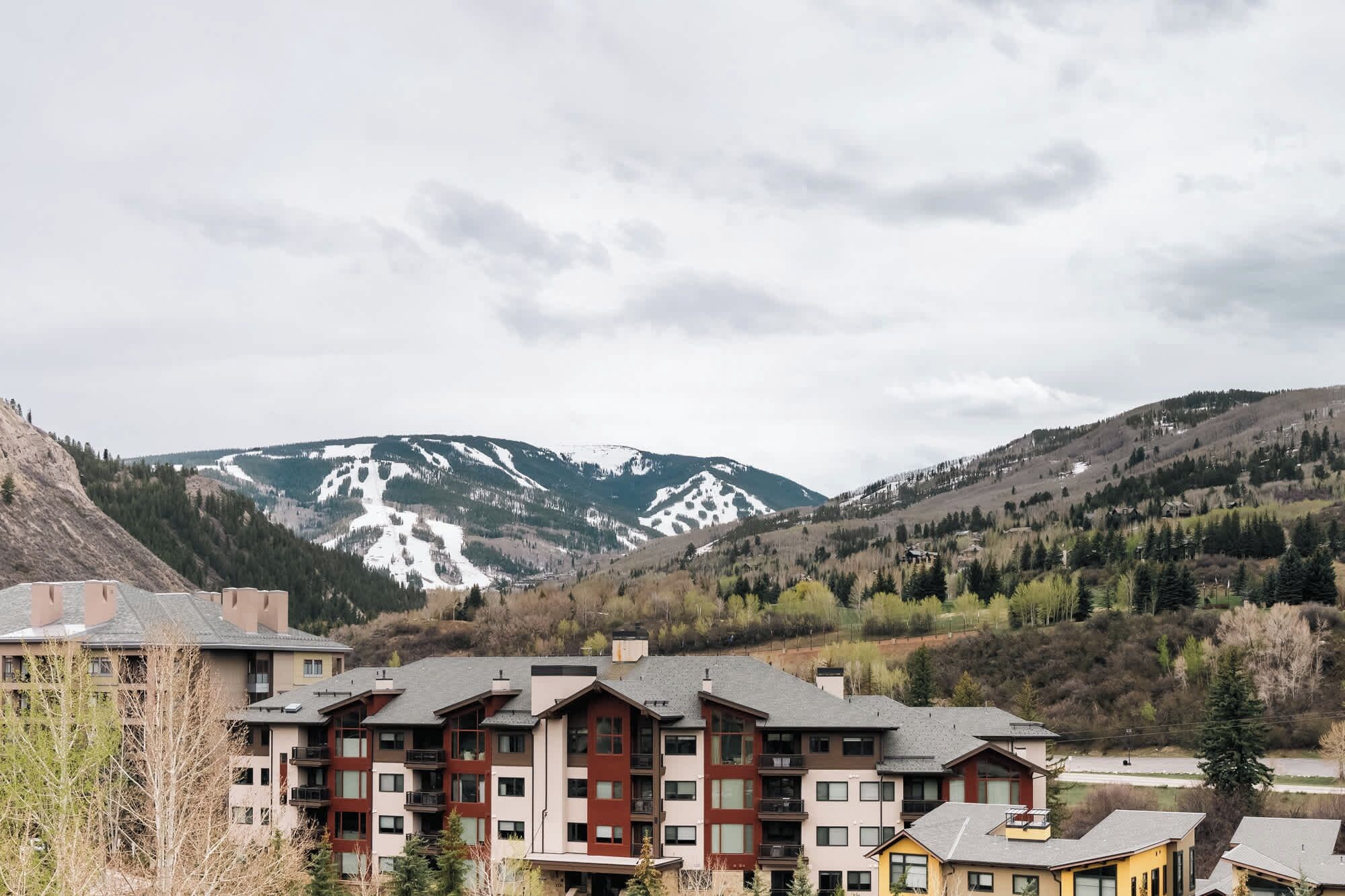 Un immeuble à plusieurs étages, doté d’une architecture moderne, avec des balcons et de grandes fenêtres, situé dans une région montagneuse où l’on aperçoit, au loin, des sommets enneigés.