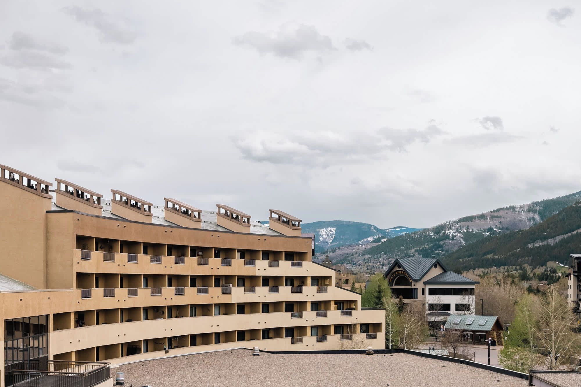 Un hôtel à plusieurs étages, doté d’un toit plat et de balcons, qui se dresse sur un fond de paysage montagneux.