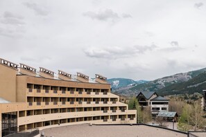 Een hotel met meerdere verdiepingen, een plat dak en balkons, gelegen tegen een bergachtige achtergrond.