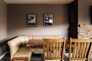 Un rincón comedor acogedor con un banco acolchado y sillas de madera, una chimenea de piedra y dos carteles enmarcados en la pared.