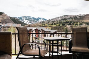 Een balkon met stoelen en een tafel, met uitzicht op een bergachtig landschap en gebouwen op de achtergrond.
