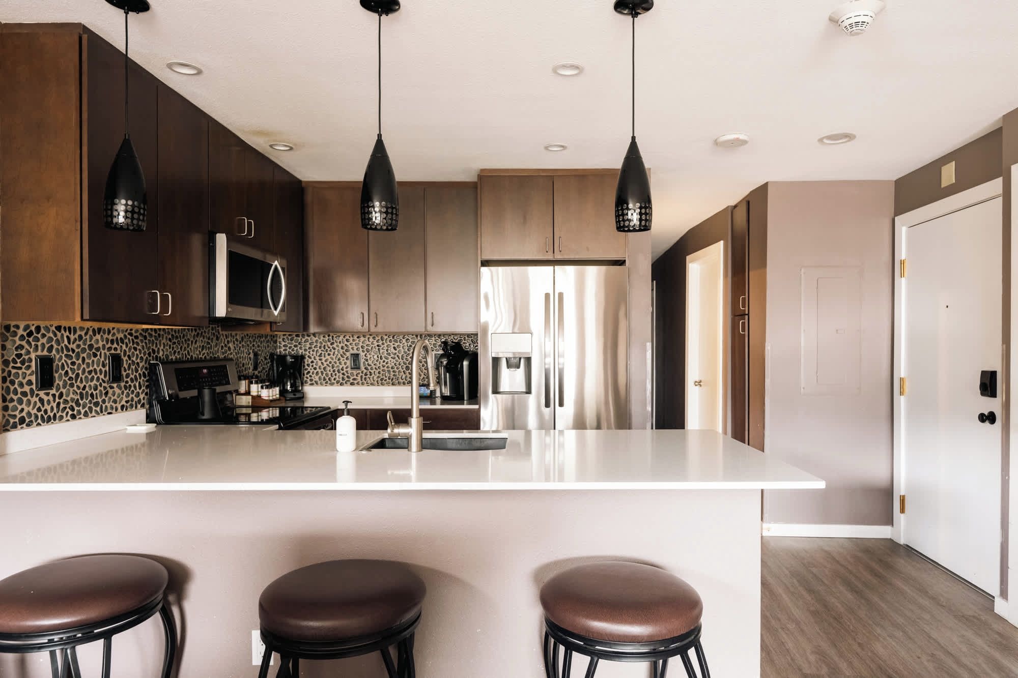 Una cocina moderna con una isla central, armarios de madera oscura e iluminación colgante.