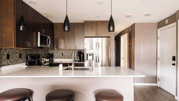 Una cocina moderna con una isla central, armarios de madera oscura e iluminación colgante.