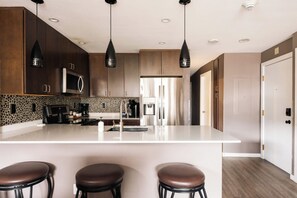 A modern kitchen with a central island, dark wooden cabinets, and pendant lighting. - Choice Condo | Walk to Gondola | Sleeps 7! (Avon)