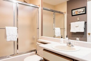 Un baño moderno con cabina de ducha de vidrio, un lavabo blanco con espejo y un perchero con toallas blancas.