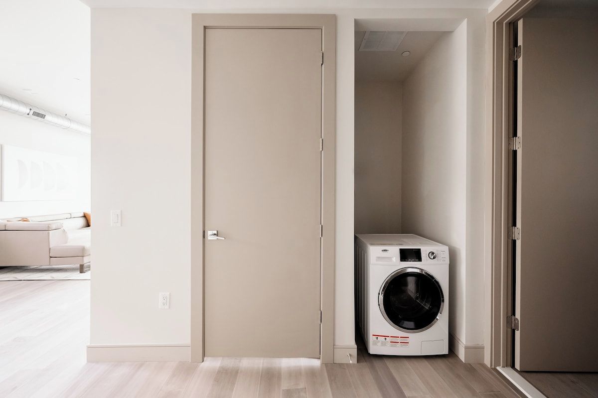 A laundry room with a washing machine, a door, and a light-colored floor.