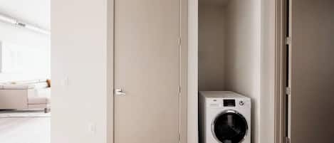 Un lavadero con lavadora, una puerta y piso de color claro.