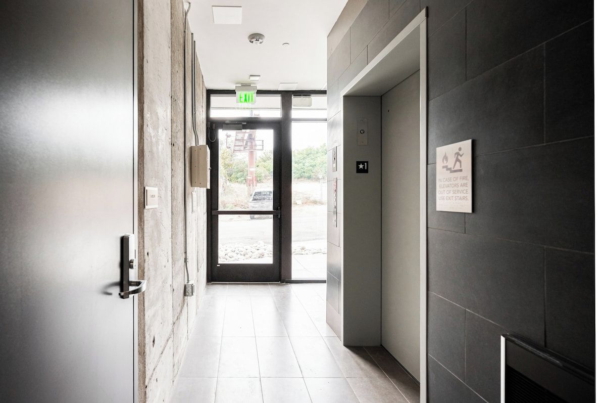 A hallway with a door leading to an outdoor area, a fire exit sign, and a sign indicating elevator out of service.