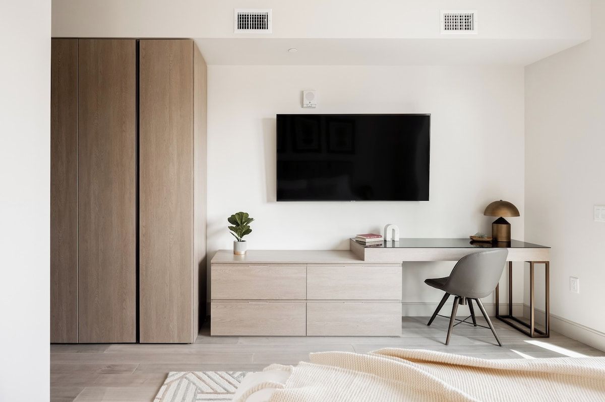 A modern room with a large wardrobe, a desk with a chair, a flat-screen TV, and a small plant.