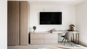 A modern room with a large wardrobe, a desk with a chair, a flat-screen TV, and a small plant.