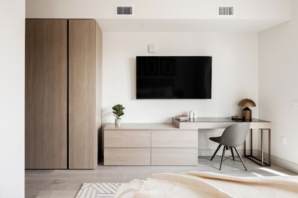 A modern room with a large wardrobe, a desk with a chair, a flat-screen TV, and a small plant.