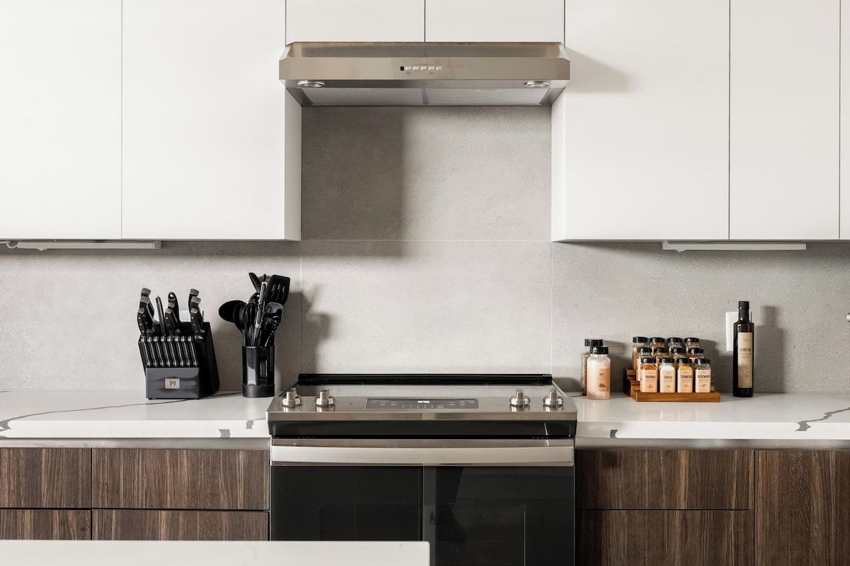 A kitchen with a stove, oven, and cabinets. There are knives in a holder and bottles on the counter.