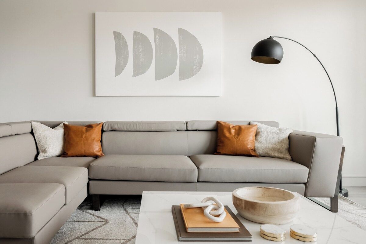 Ein modernes Wohnzimmer mit einem Ecksofa, einem Couchtisch, einer Stehlampe und einem an der Wand befestigten abstrakten Kunstwerk.