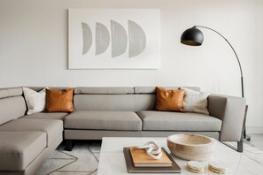A modern living room with a sectional sofa, a coffee table, a floor lamp, and a wall-mounted abstract art piece.