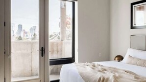 Um quarto com cama, uma janela grande e vista para a cidade.