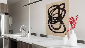 A modern kitchen with a central island, a stainless steel refrigerator, and a large abstract painting on the wall.