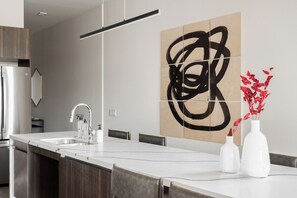 A modern kitchen with a central island, a stainless steel refrigerator, and a large abstract painting on the wall.
