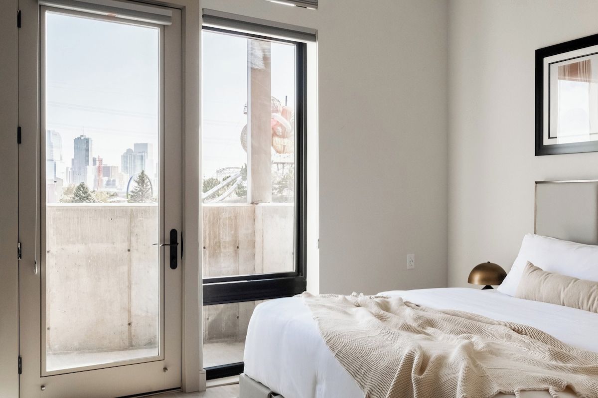 Ein Schlafzimmer mit einem Bett, einem Fenster und Blick auf eine Stadtlandschaft.