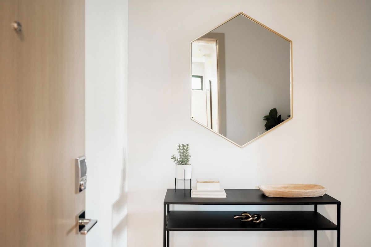 A modern interior with a black console table, a geometric mirror, and a potted plant.