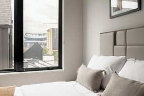 A bedroom with a bed, pillows, a window, and a view of buildings. - Penthouse Views | Walk to Empower Field | Tesoro (Denver)