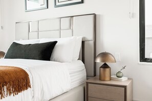 A neatly made bed with a headboard, a bedside lamp, a small vase with flowers, and a framed picture on the wall.