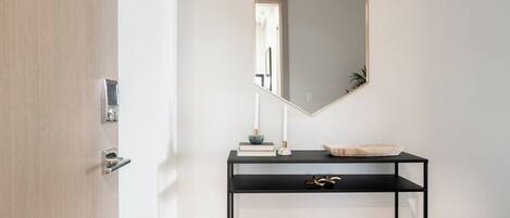 Un baño minimalista con un mueble de consola negro, un lavabo pedestal blanco y un espejo grande con marco dorado.