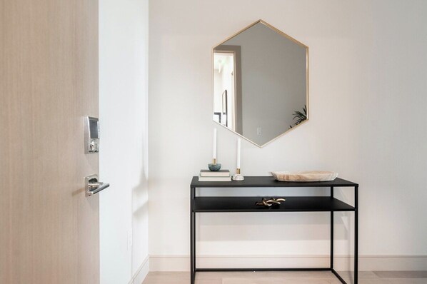 A minimalist bathroom with a black console table, a white pedestal sink, and a large mirror with a gold frame.
