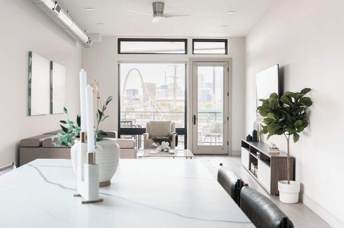 Una sala de estar moderna con comedor, ventanas amplias y vistas a un paisaje urbano.