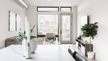 Una sala de estar moderna con comedor, ventanas amplias y vistas a un paisaje urbano.