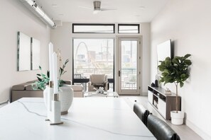 A modern living room with a dining area, large windows, and a view of a cityscape.