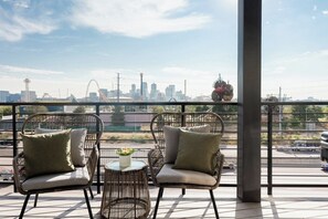 Two wicker chairs with cushions on a balcony with a city skyline view.