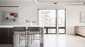 A modern kitchen with a central island, bar stools, and a large window offering a city view.