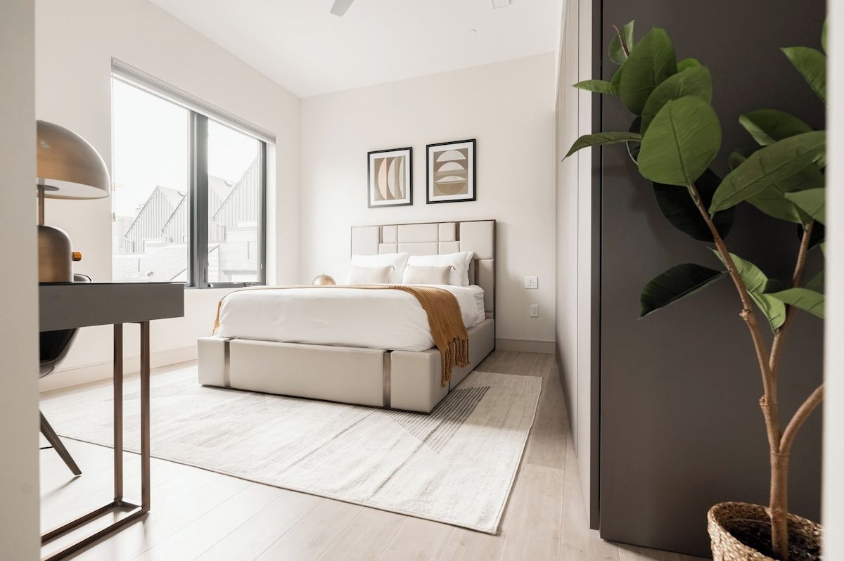 A modern bedroom with a bed, bedside table, and a large window.