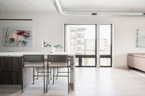 A modern kitchen with a dining area, large windows, and a view of buildings. - Penthouse Views | Walk to Empower Field | Tesoro (Denver)