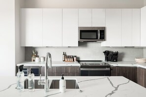 A modern kitchen with white cabinets, a stainless steel microwave, a sink with a faucet, and a marble countertop. - Penthouse Views | Walk to Empower Field | Tesoro (Denver)