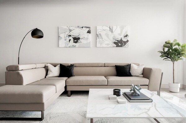 Un salon moderne avec un canapé d’angle beige, une table basse blanche et des œuvres d’art abstraites accrochées au mur.