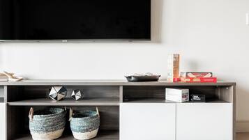 A modern living room with a flat-screen TV mounted on the wall, a wooden entertainment unit with storage, decorative items, and woven baskets.