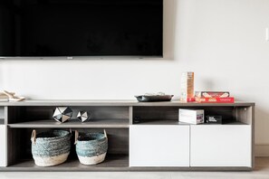 Una sala de estar moderna con un televisor de pantalla plana montado en la pared, un mueble de madera con espacio de almacenamiento, objetos decorativos y cestas tejidas.