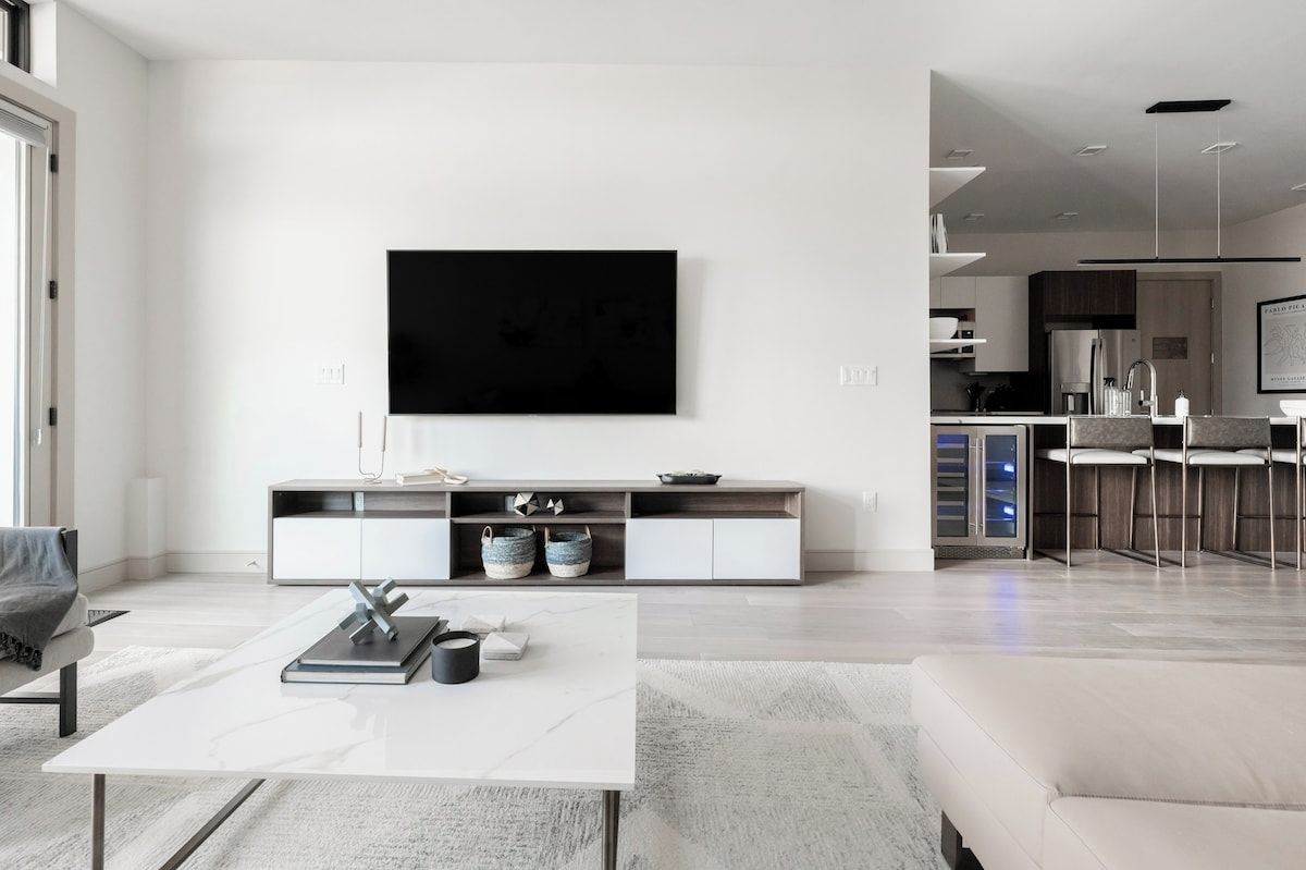 Una sala de estar moderna con un televisor de pantalla plana montado en la pared, una mesa de centro blanca y un sofá.