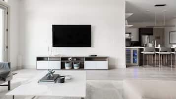 Una sala de estar moderna con un televisor de pantalla plana montado en la pared, una mesa de centro blanca y un sofá.