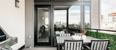 Un balcón con una parrilla, una mesa con sillas y vistas a la ciudad.