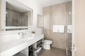 A modern bathroom with a white vanity, a large mirror, a toilet, and a glass shower enclosure.