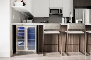 A modern kitchen with a built-in microwave, a refrigerator, and a glass-fronted mini-fridge.