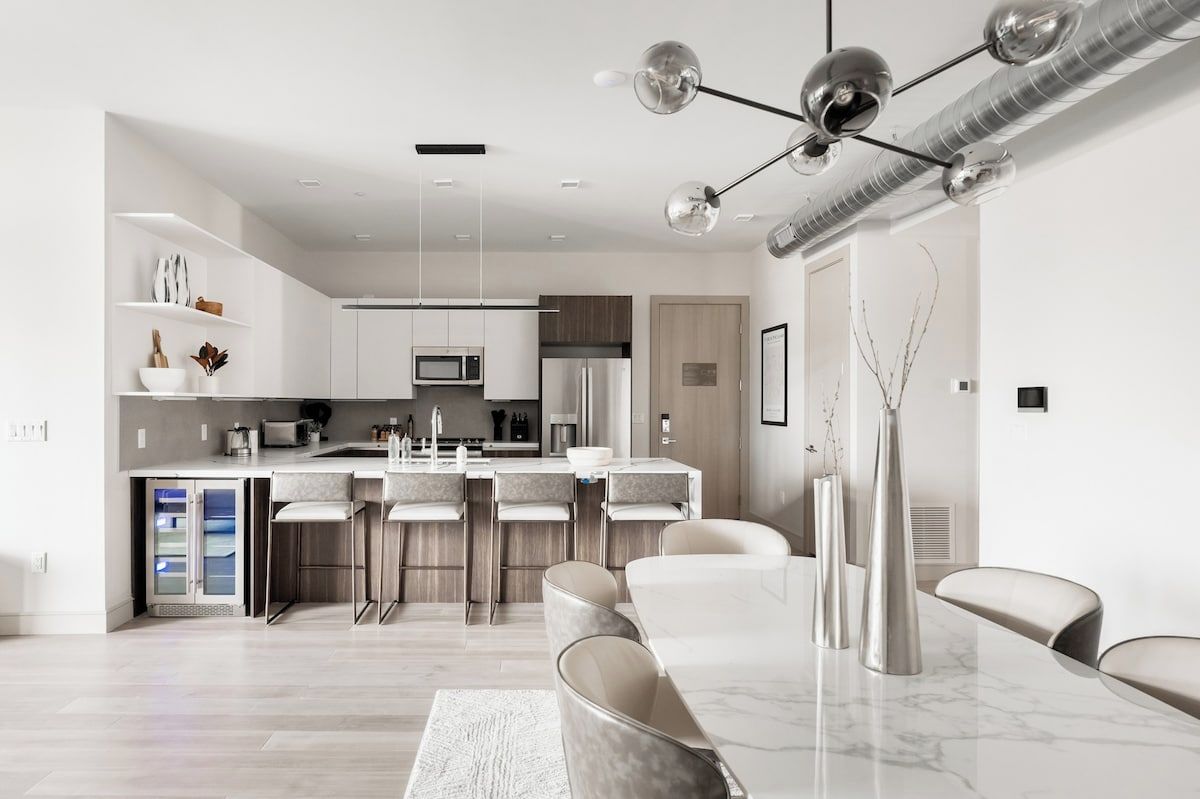 Cozinha moderna com ilha central, banquetas de bar e mesa de jantar com cadeiras.