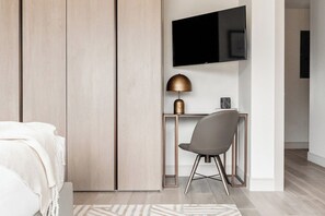 A modern bedroom with a bed, a desk, and a TV mounted on the wall.