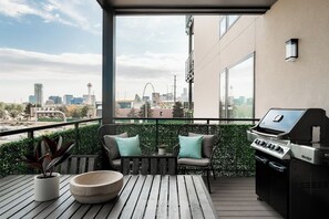 A balcony with a grill, seating, and a view of a cityscape.