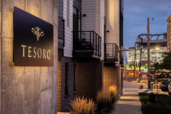 A sign for 'TESORO' on a building facade with a modern design, a brick wall, and a balcony.