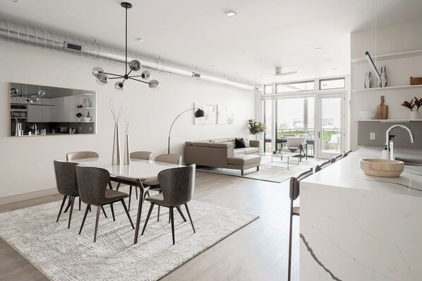 A modern kitchen with a white countertop, a sink, and a dining area with a table and chairs.