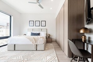 A modern bedroom with a bed, bedside table, lamp, and a view of the city.